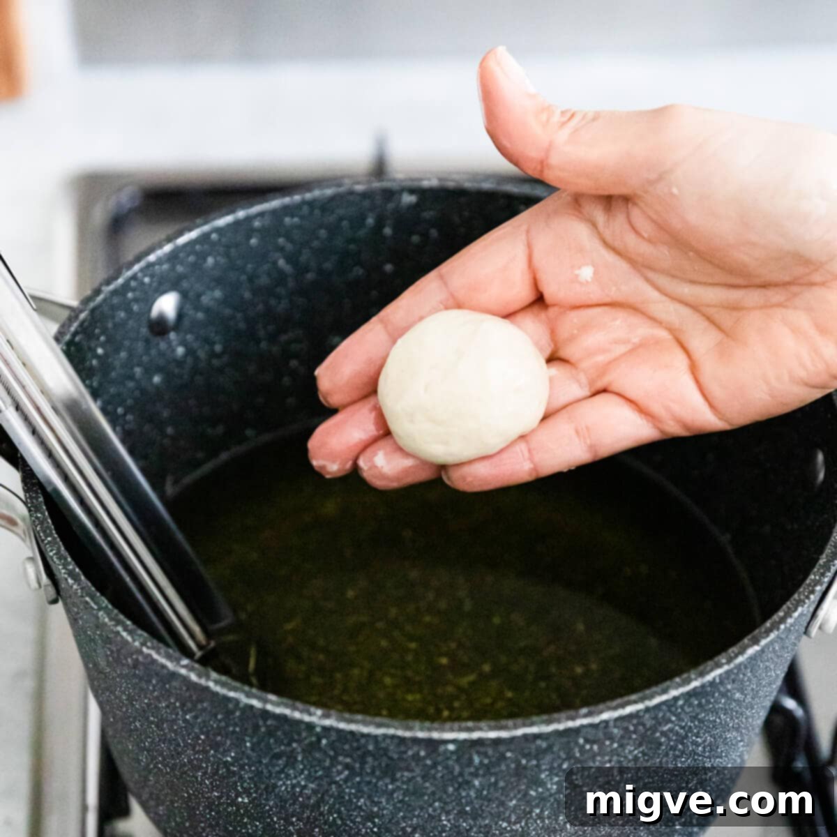doughnut dough ball being held above the cooing oil.