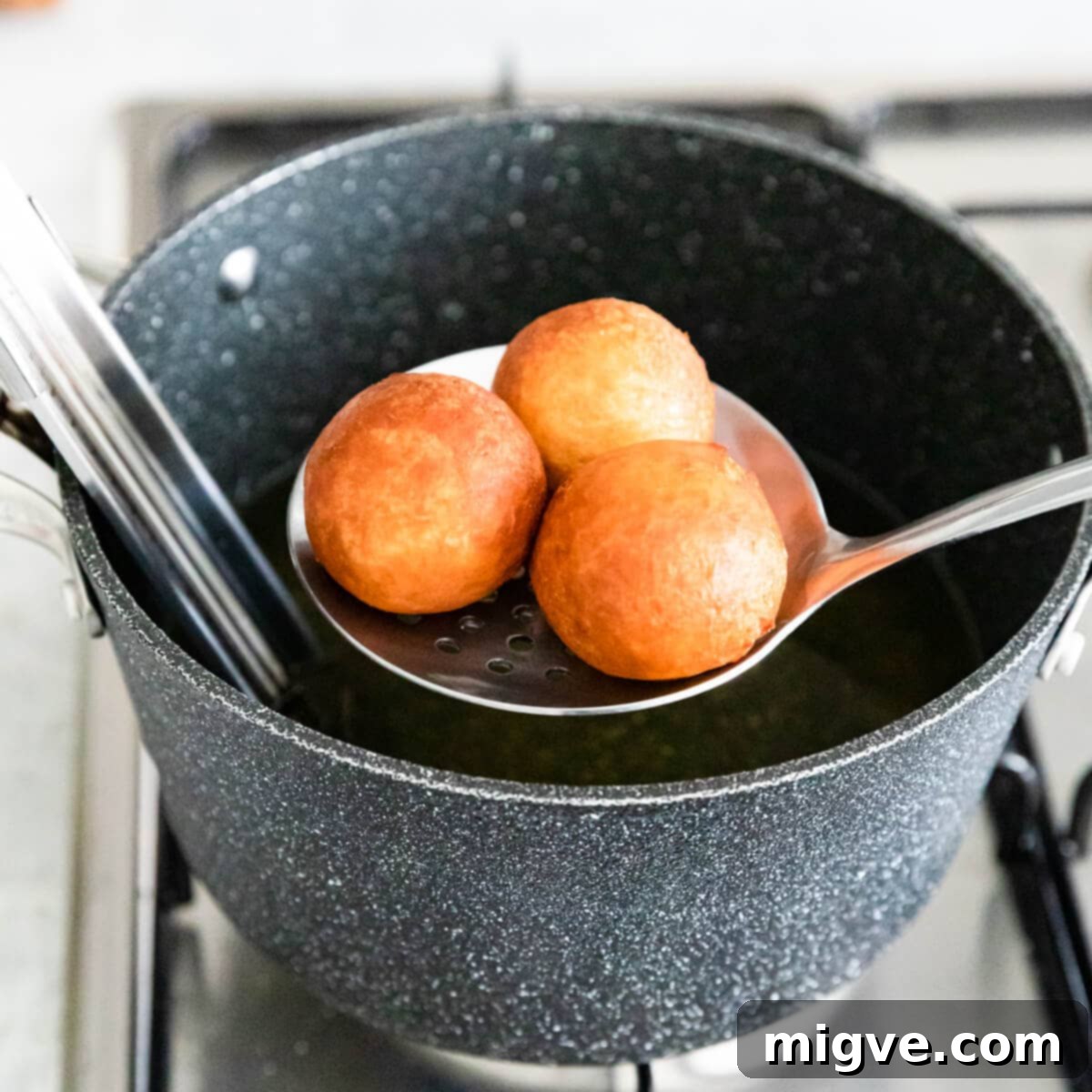 donut holes being taken out of the hot oil with slotted spoon.