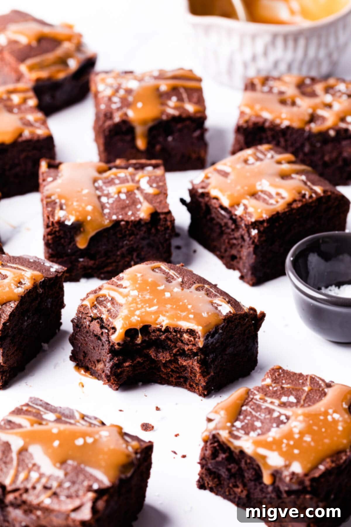 square pieces of brownies drizzled with salted caramel with one brownie missing a bite.