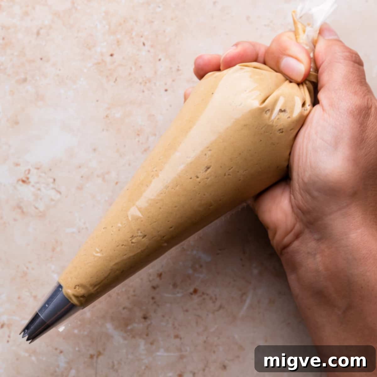 A transparent piping bag neatly filled with gingerbread buttercream, ready for macaron assembly.