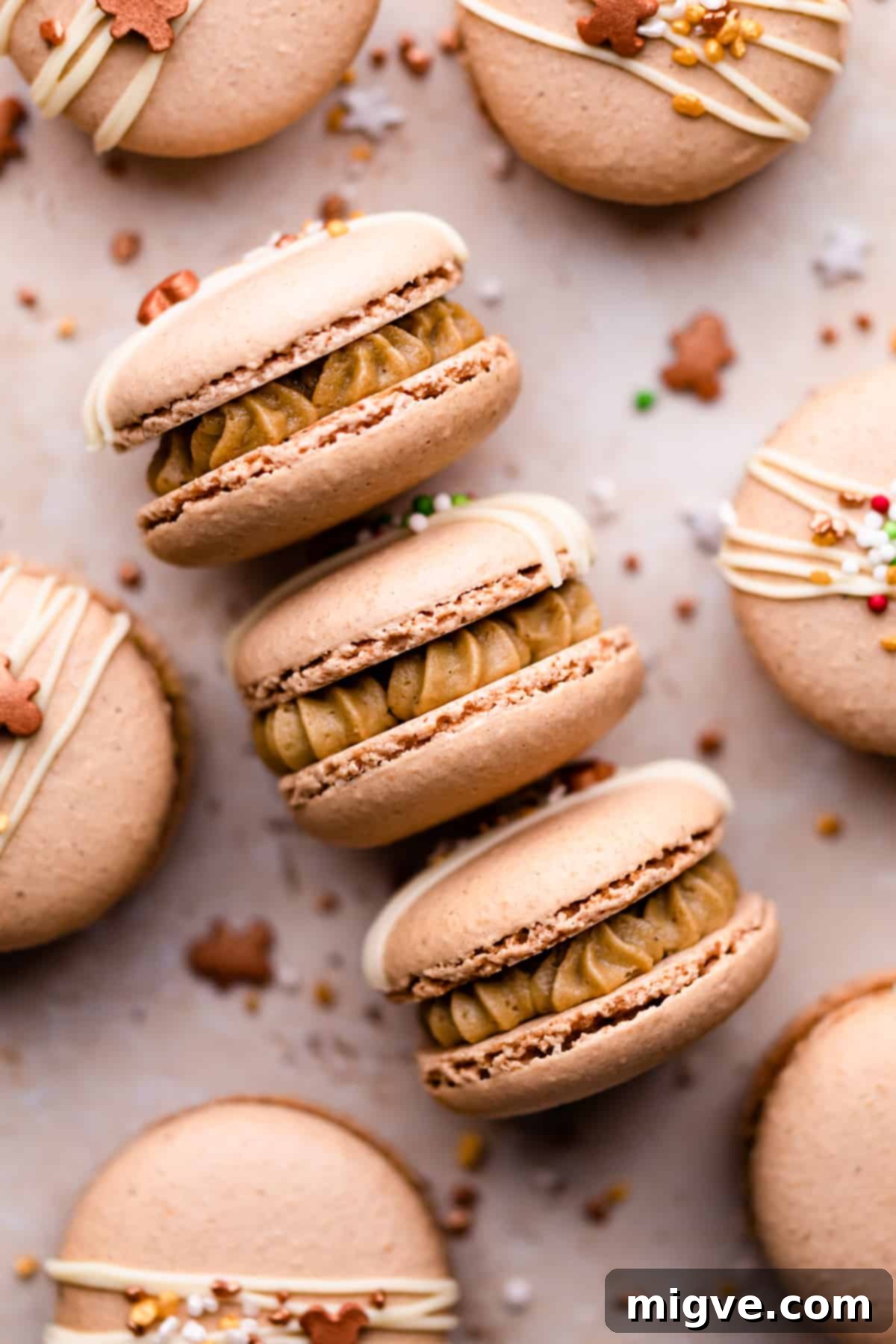 Three perfectly filled gingerbread macarons resting on a flat surface, surrounded by scattered festive sprinkles.
