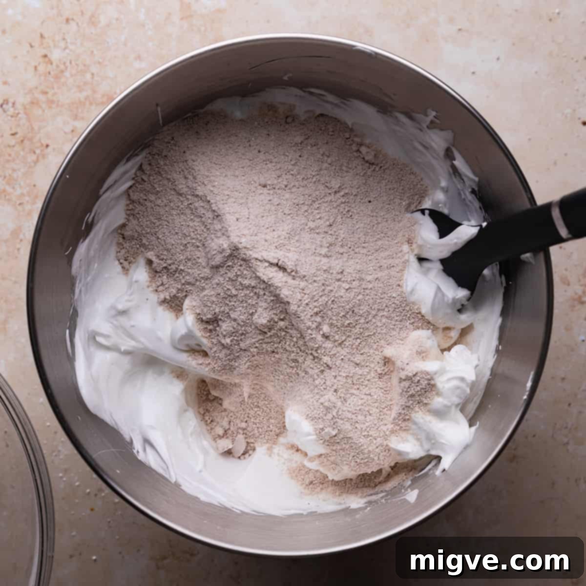 Dry ingredients gently folded into meringue in a metal mixing bowl with a spatula.
