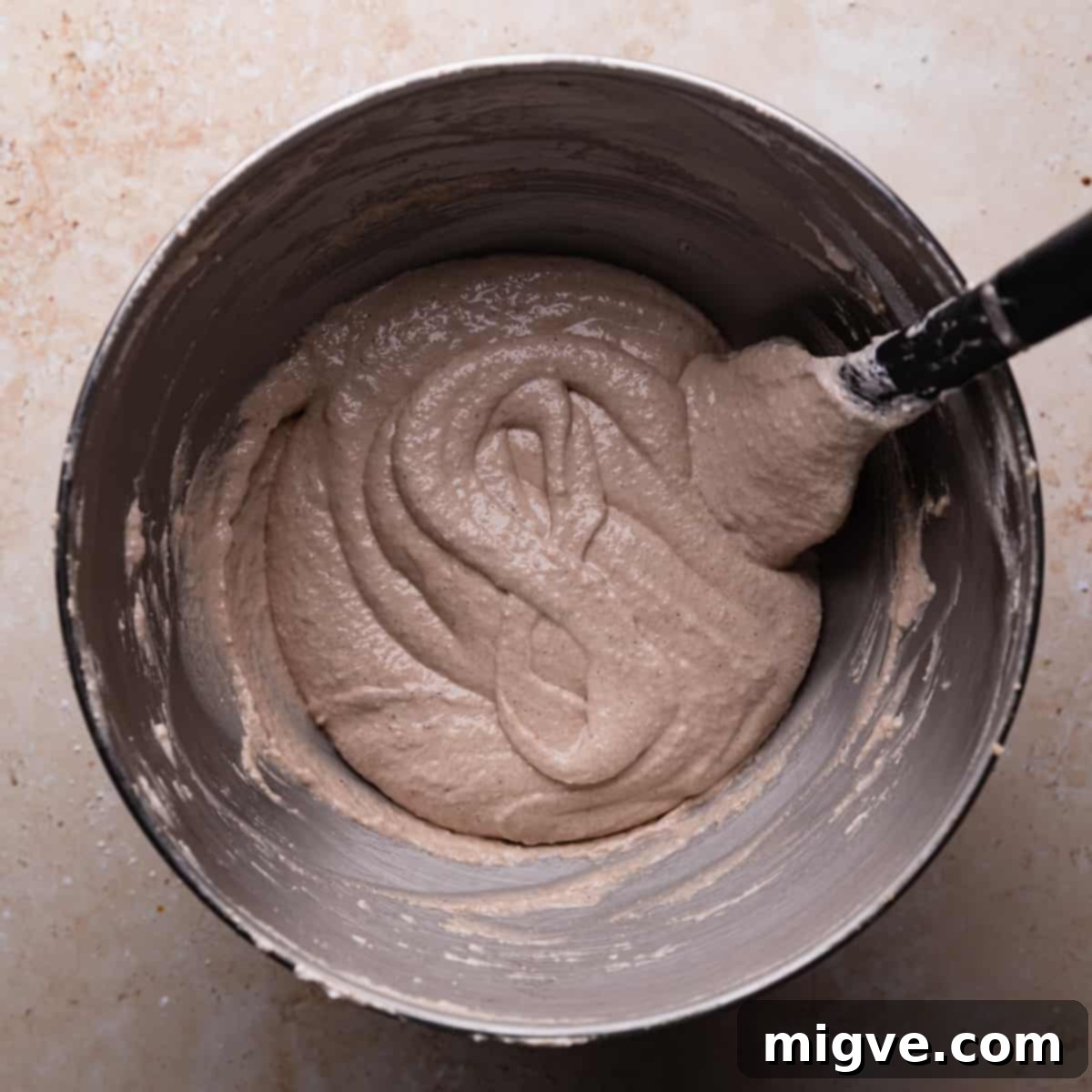 A figure '8' traced in gingerbread macaron batter within a metal mixing bowl, demonstrating the correct consistency.