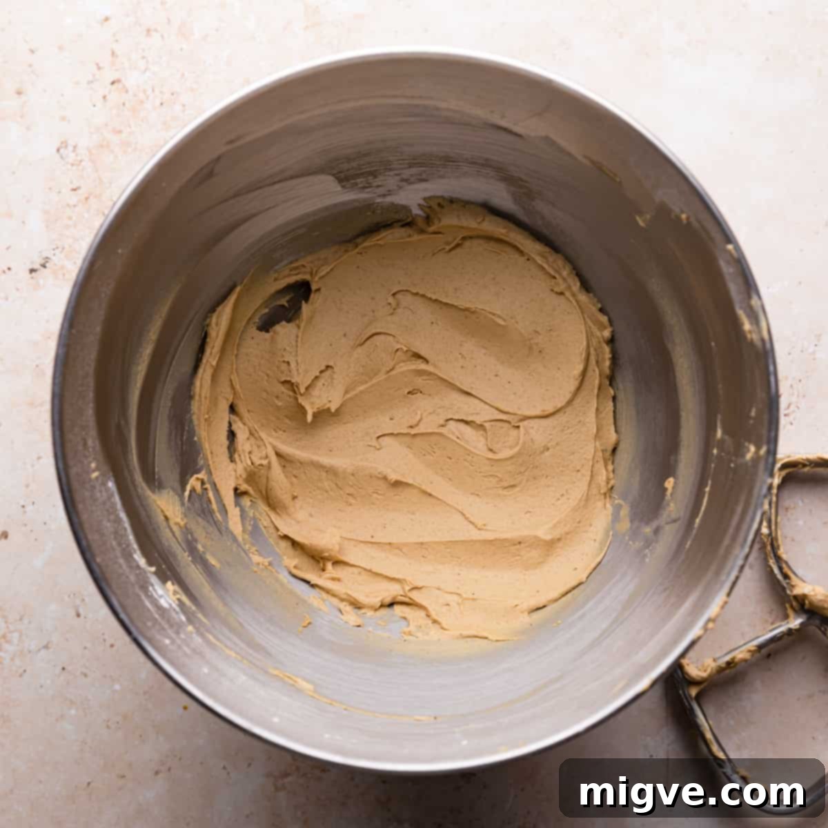 A metal mixing bowl containing freshly made, creamy gingerbread buttercream.