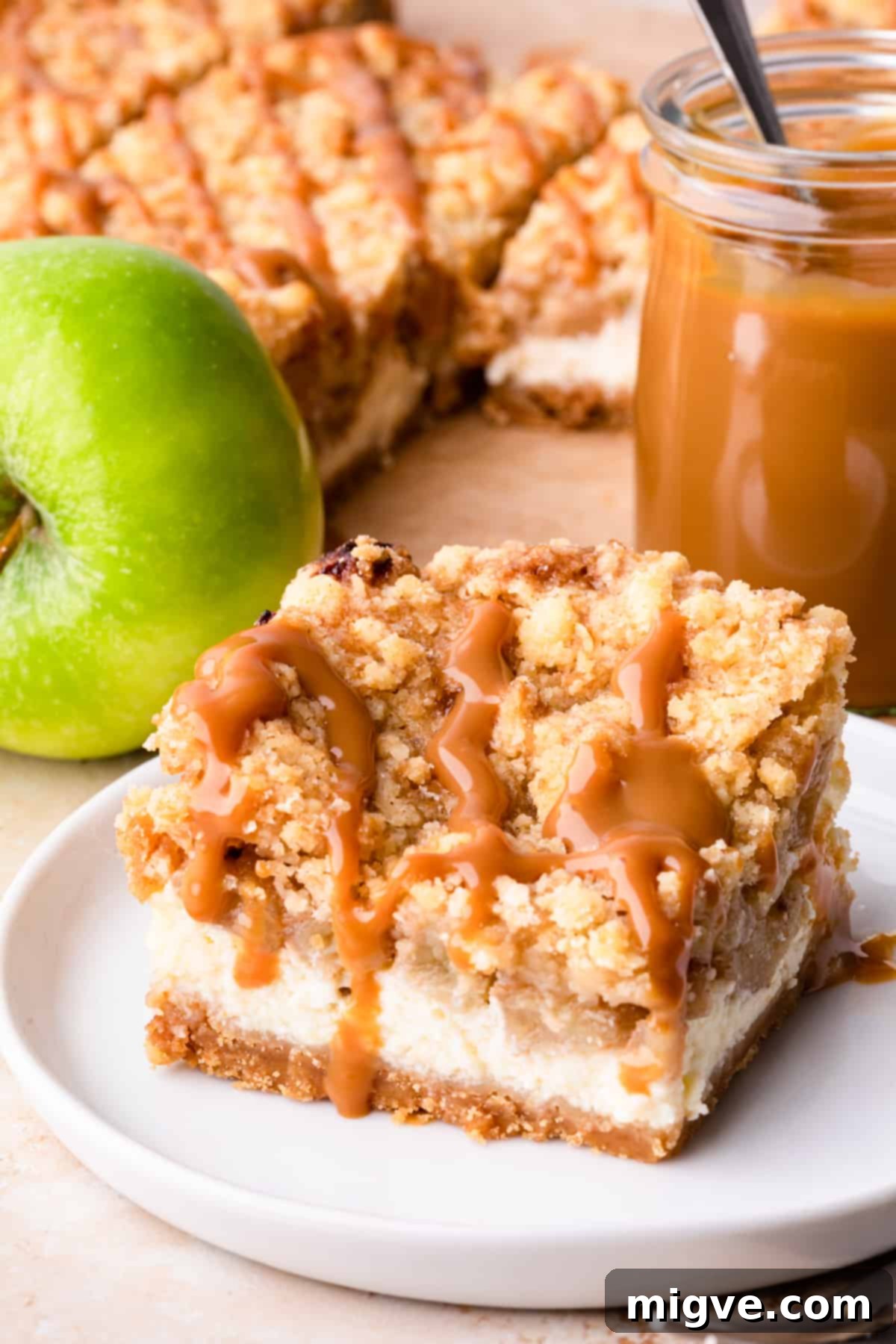 A beautifully composed image of homemade caramel apple cheesecake bars, showcasing their distinct layers: golden crust, creamy cheesecake, spiced apple, and crumble, topped with caramel drizzle. Perfect for a cozy autumn treat.