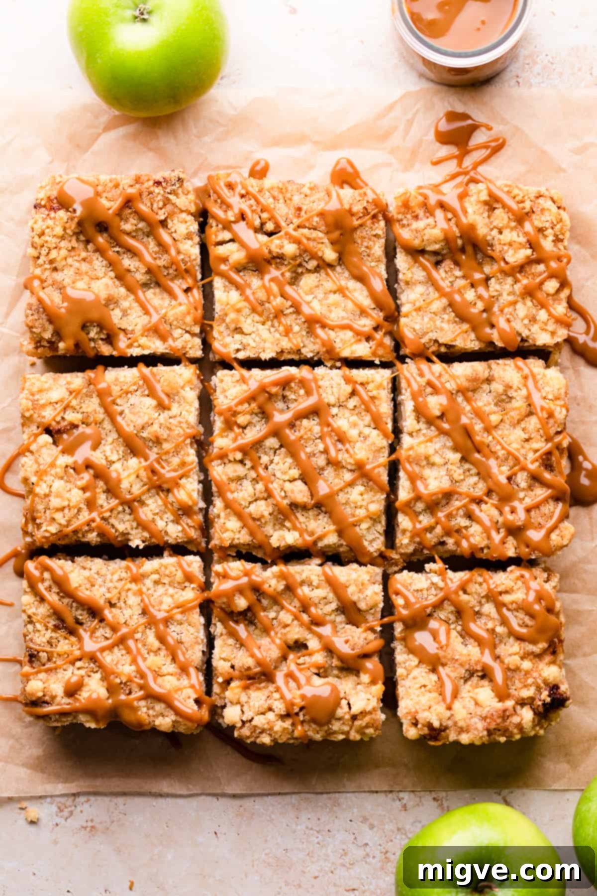 A serving tray displaying nine perfectly sliced caramel apple cheesecake bars, each piece individually drizzled with warm, glistening caramel sauce, ready to be enjoyed.