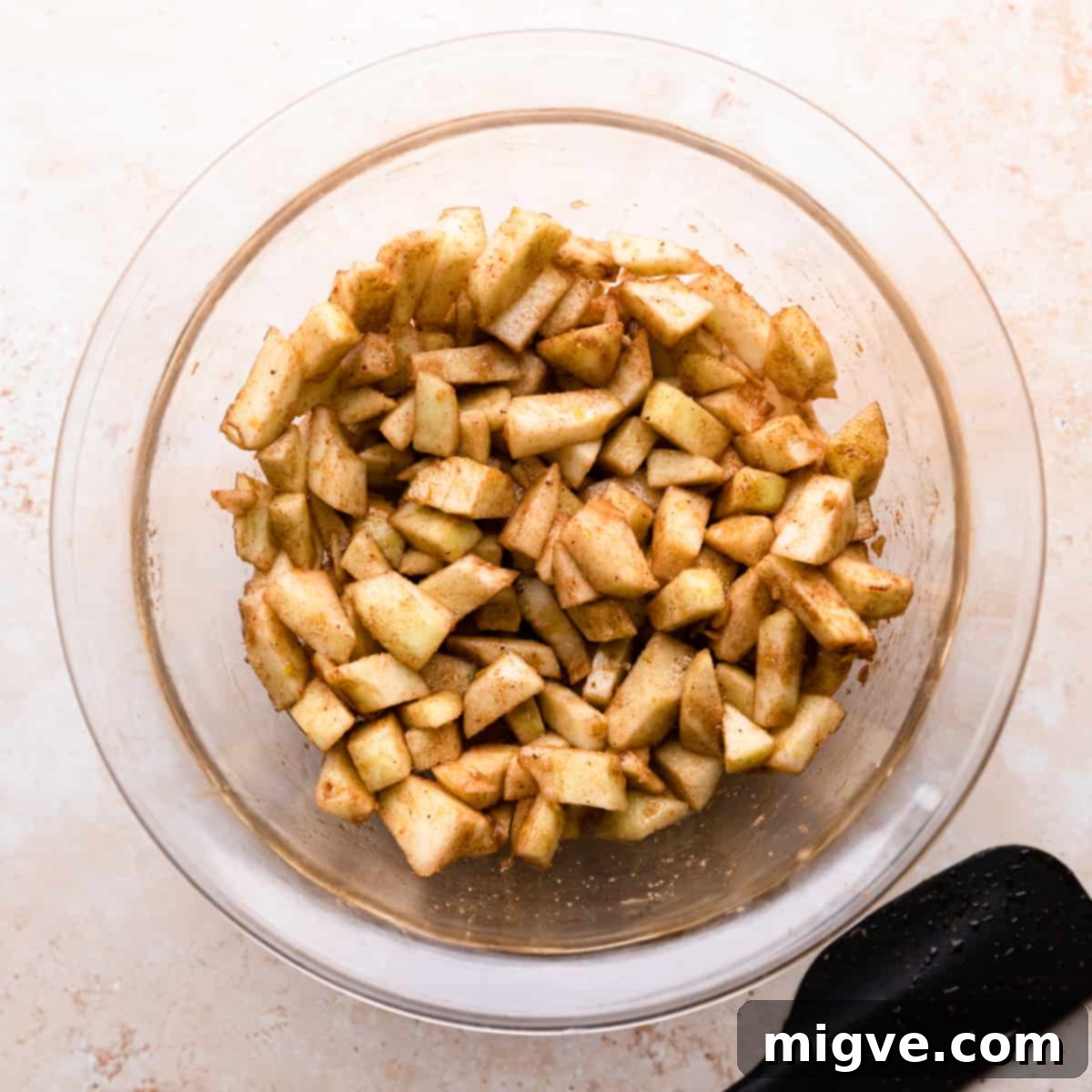 A mixing bowl filled with freshly chopped apples, generously coated in warming spices and a hint of lemon zest, ready for the apple cheesecake bar layers.