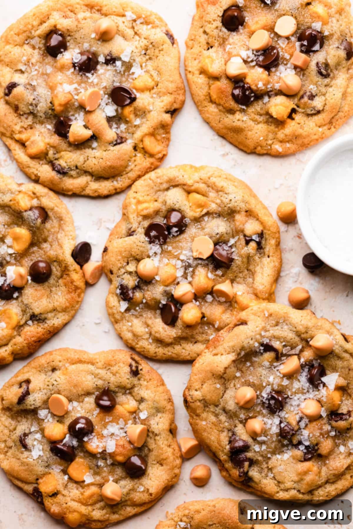 batch of butterscotch chocolate chip cookies with sea salt and some more butterscotch and chocolate chips surrounding them.