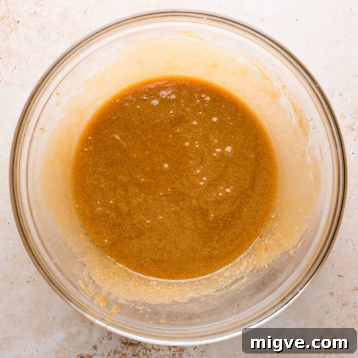 large glass bowl with mixture of melted butter, brown sugar and egg and vanilla.