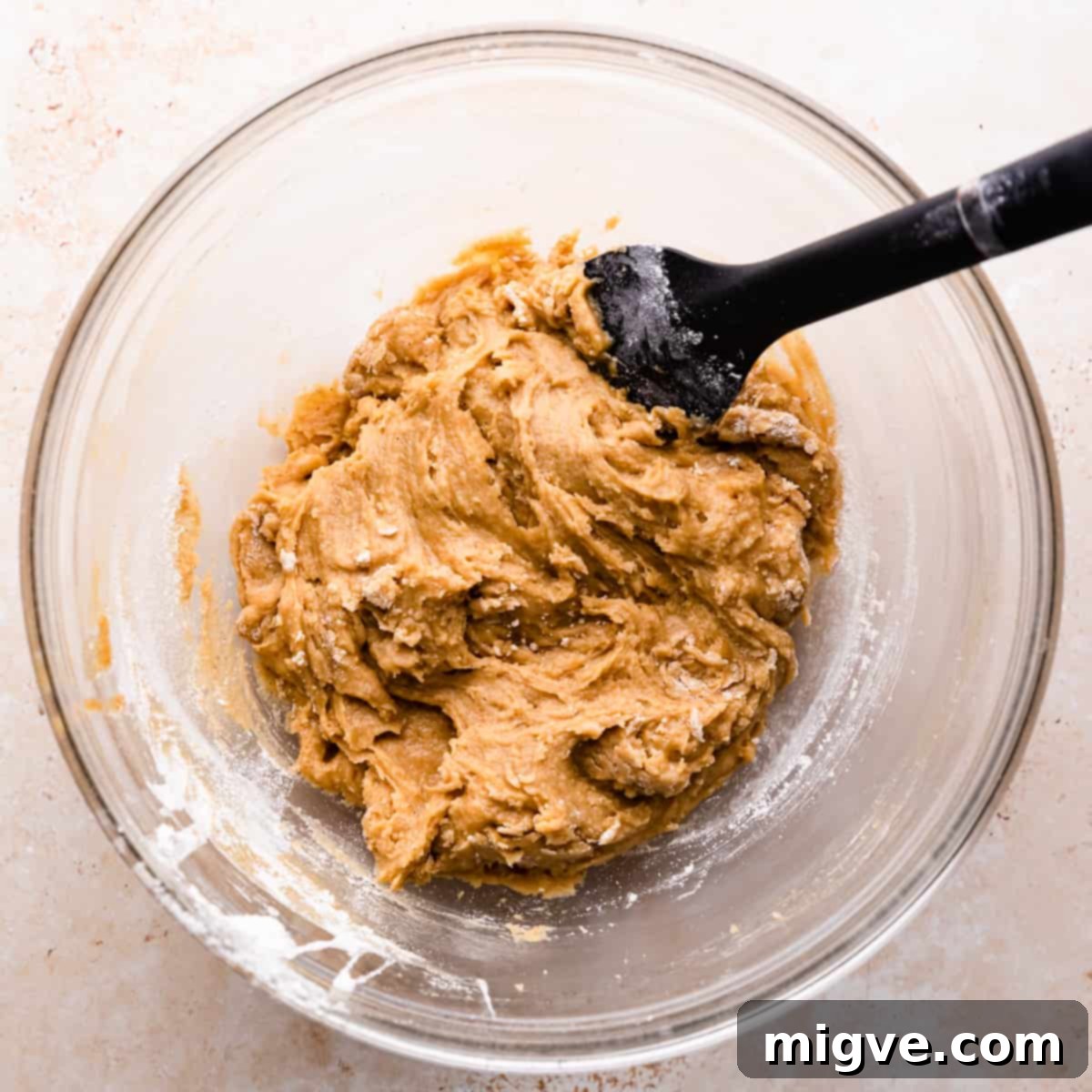 glass bowl with plain cookie dough and black silicone spatula inside it.