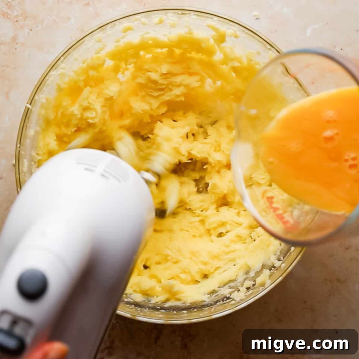 bowl with creamed butter and sugar and eggs being poured into it while mixing with electric mixer.
