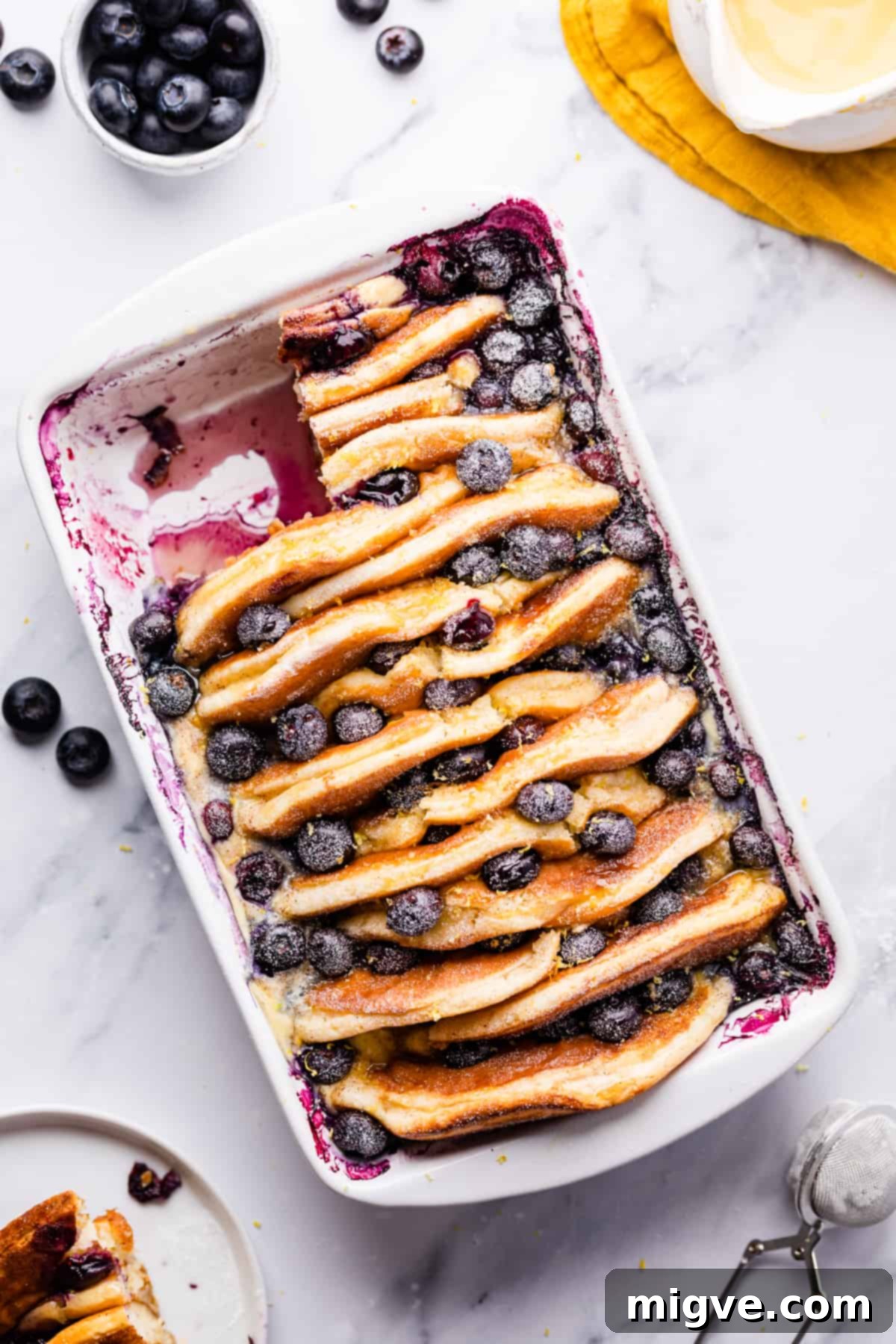 Baked Blueberry Pancake Bliss 2 Blueberry Pancake Pudding dusted with icing sugar, with a portion cut out, showcasing its delicious layers.