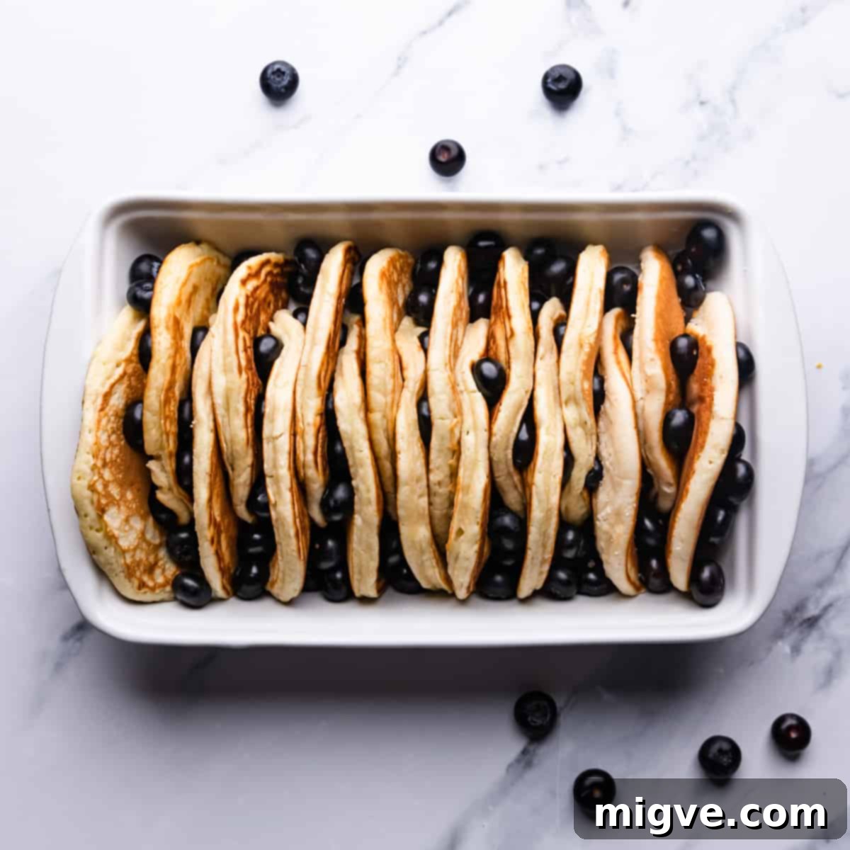 Baked Blueberry Pancake Bliss 6 Ceramic baking dish filled with neatly arranged pancake halves and scattered fresh blueberries.