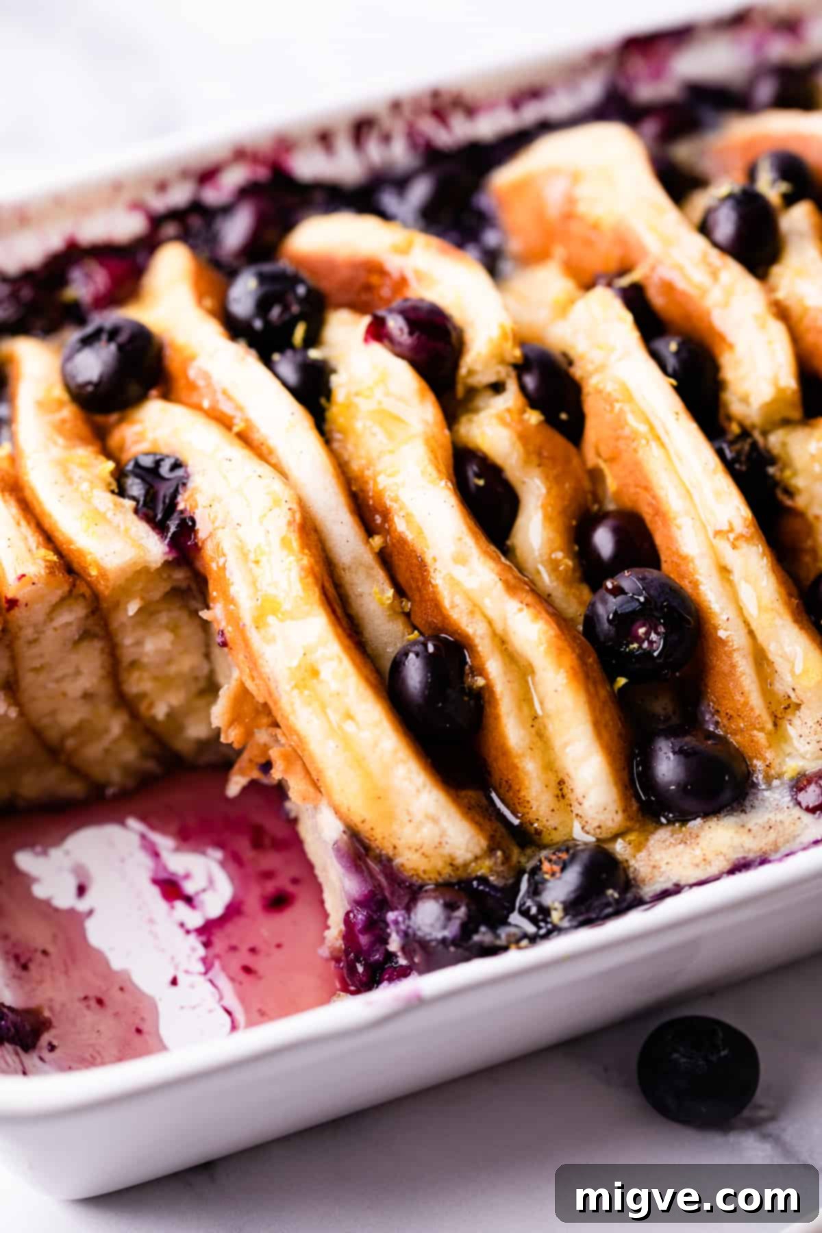 Baked Blueberry Pancake Bliss 9 Close-up of baked pancake pudding with blueberries and eggy custard inside a baking dish, with a serving removed.