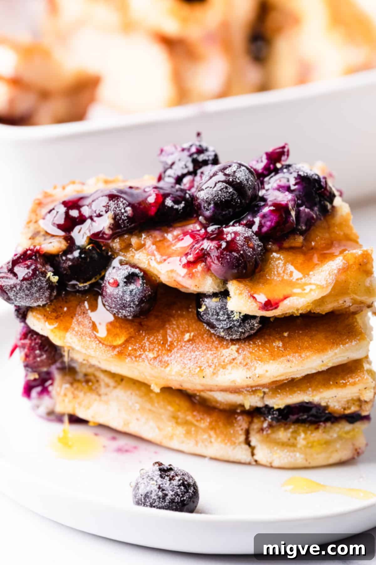 Baked Blueberry Pancake Bliss 10 A portion of blueberry pancake pudding drizzled with honey and garnished with extra fresh blueberries on a small white plate.