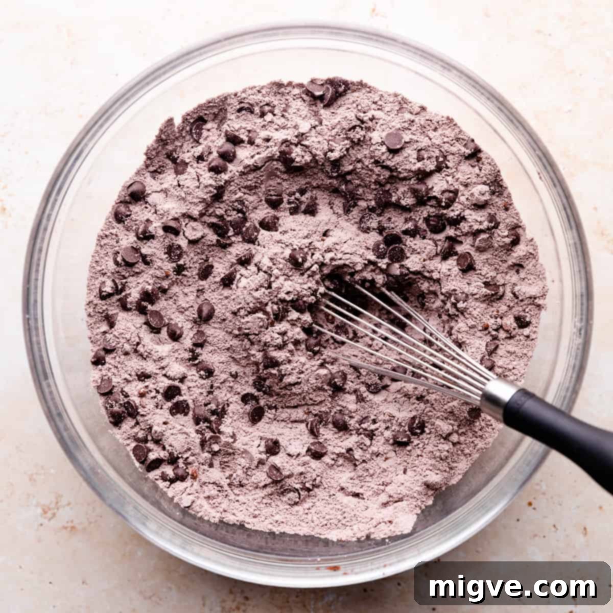 A clear glass mixing bowl filled with dry ingredients and an abundance of chocolate chips, ready for mixing.