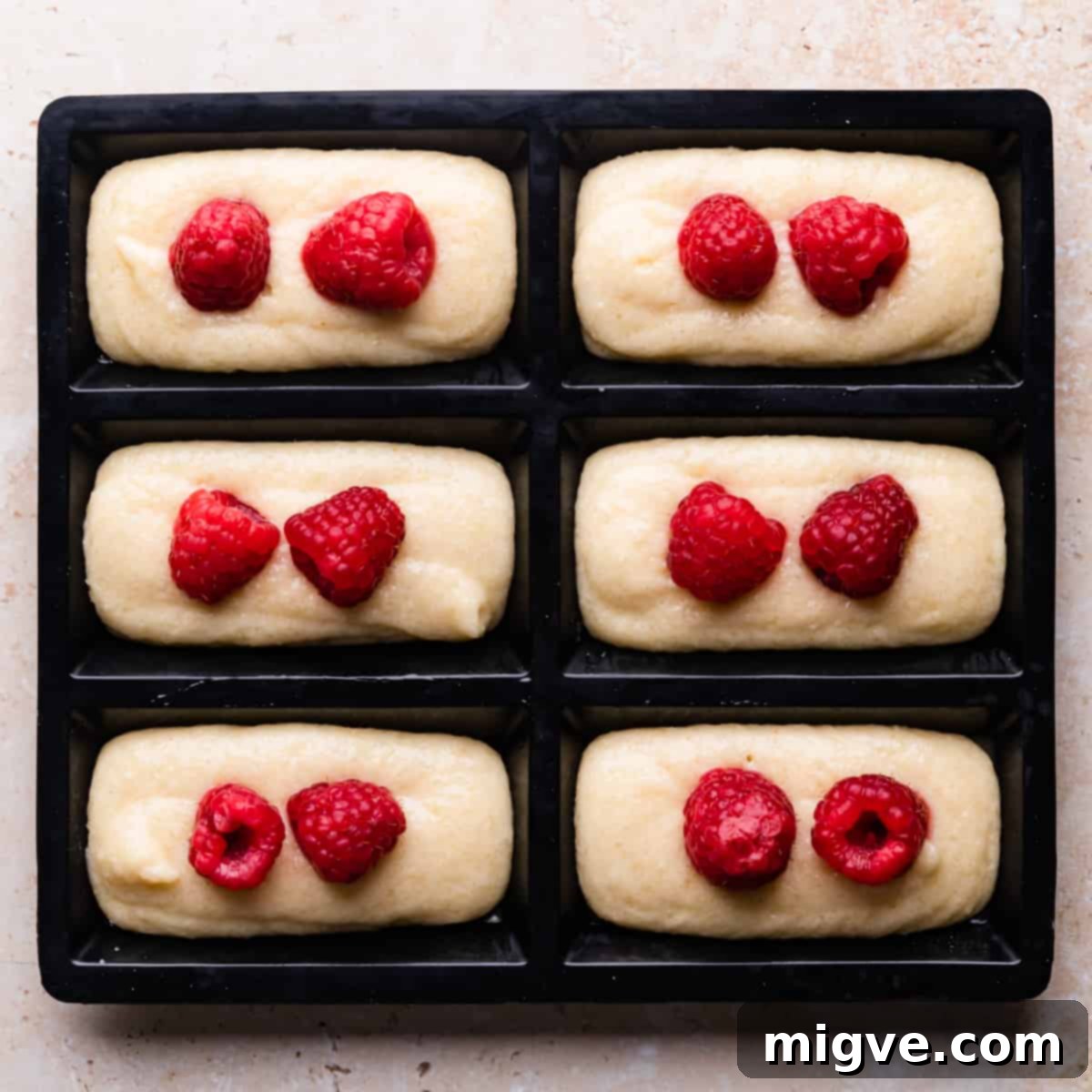 silicone mould for financiers filled with cake batter and topped with raspberries.