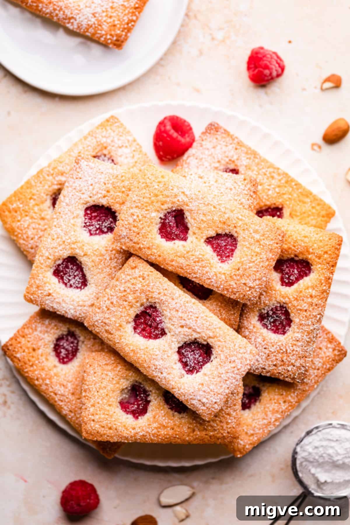 small rectangular financier cakes with raspberries and icing sugar on a white plate.