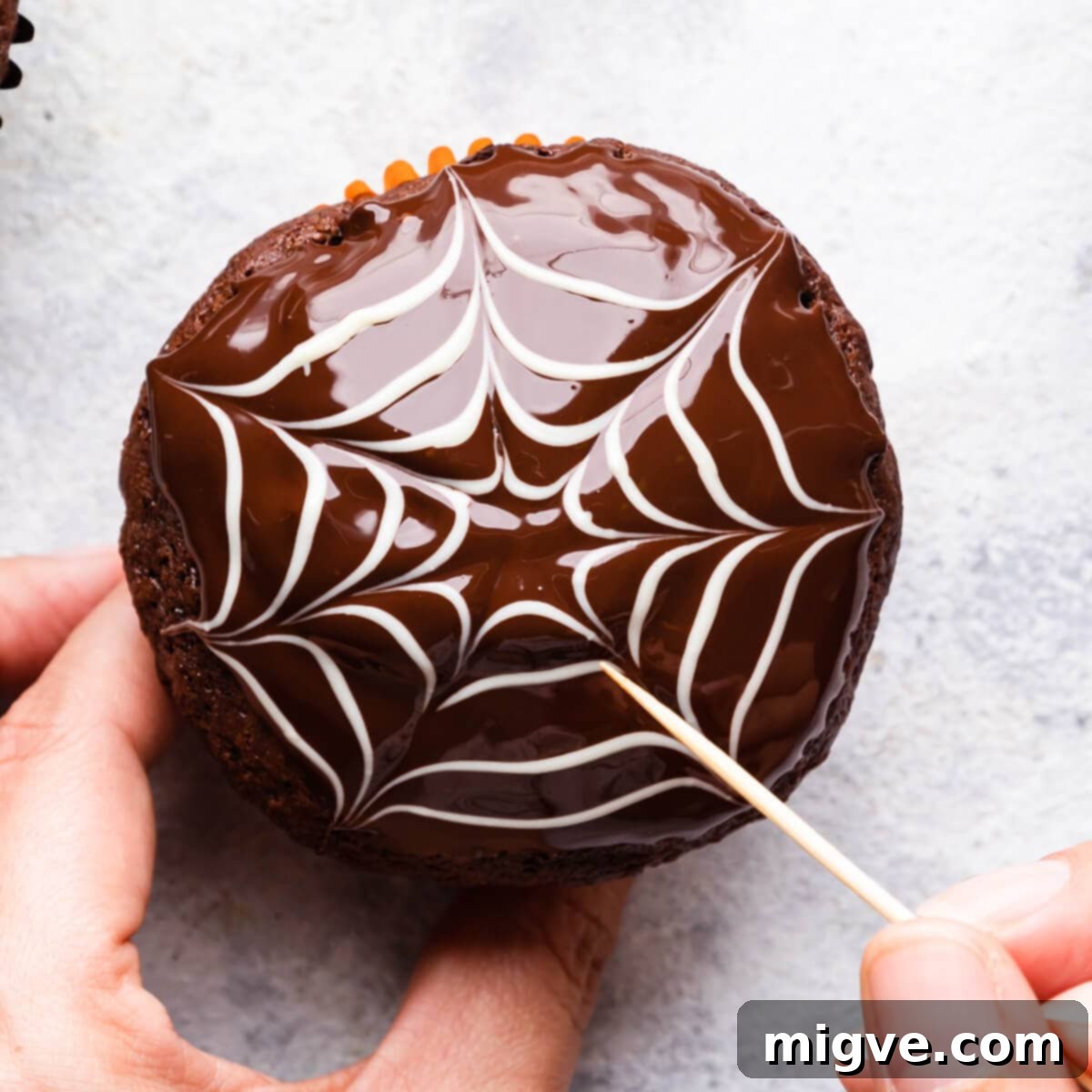 A chocolate muffin with a partially completed spiderweb design, showing lines drawn through the white chocolate circles.