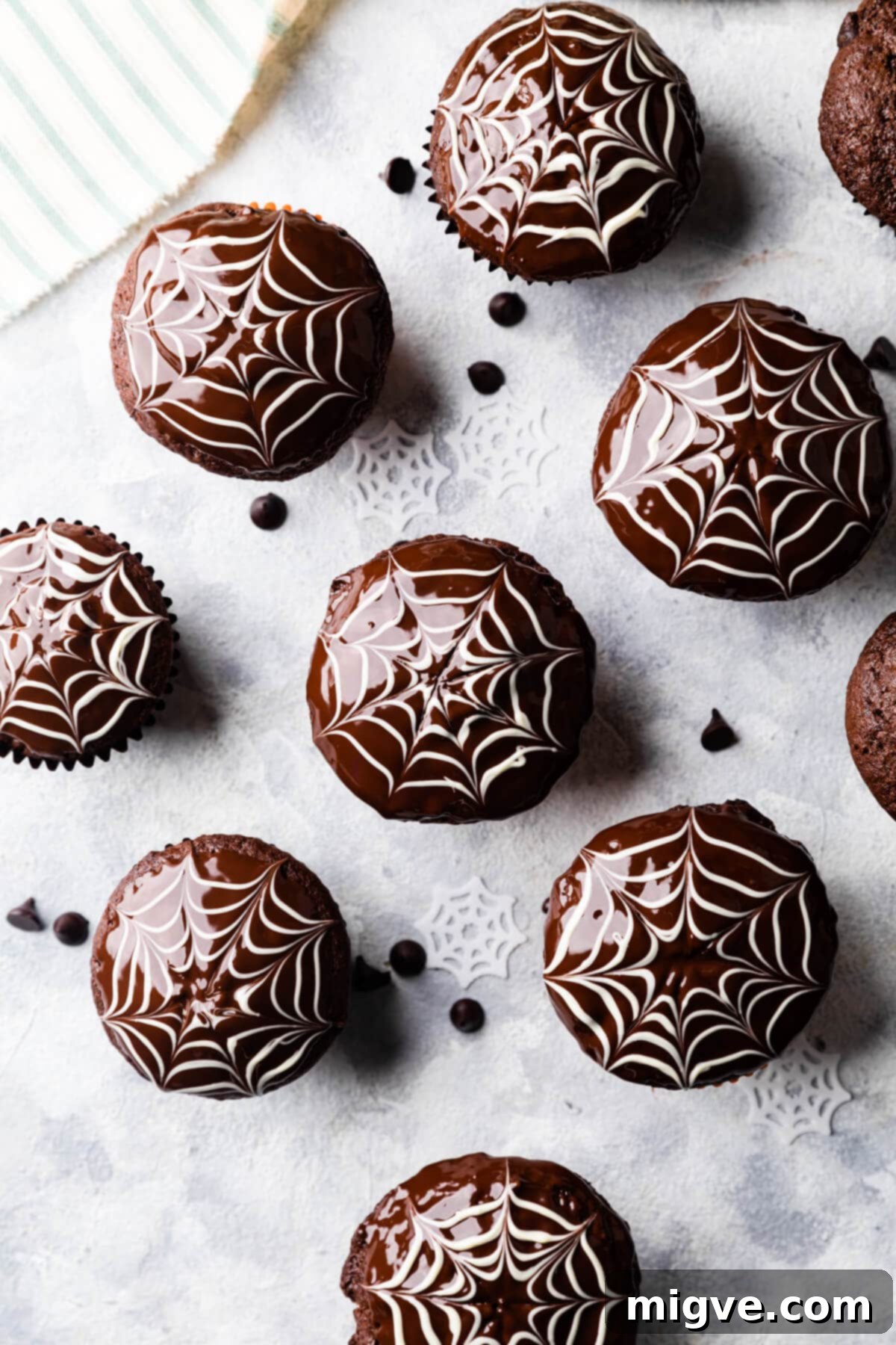 A charming batch of chocolate fudge muffins, each adorned with an edible chocolate spiderweb decoration, presented in bright orange cases.