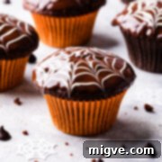 A single chocolate fudge spiderweb muffin, beautifully decorated and presented in a bright orange muffin case.
