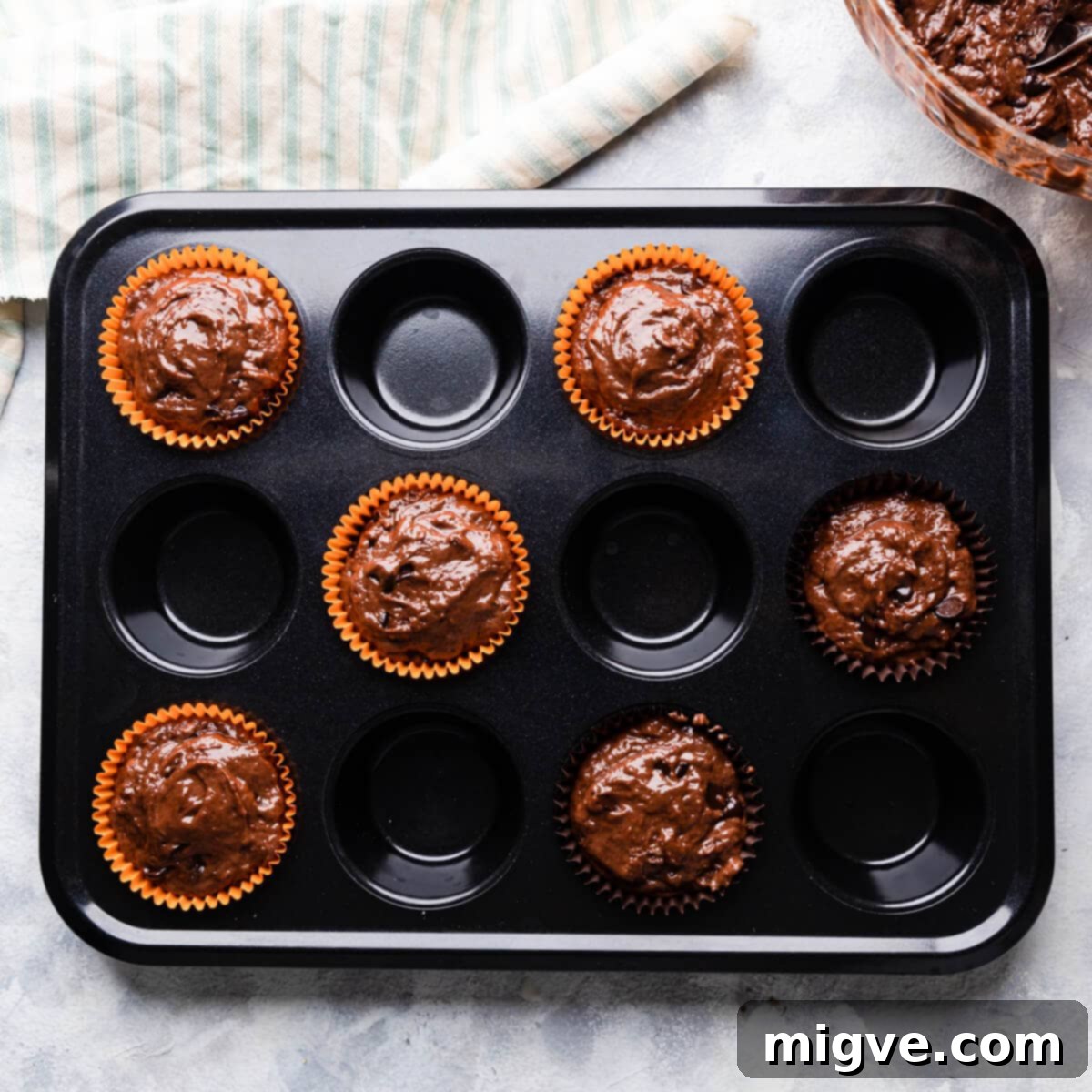 A muffin tin with six paper cases, each filled with the rich chocolate muffin batter, ready for baking.