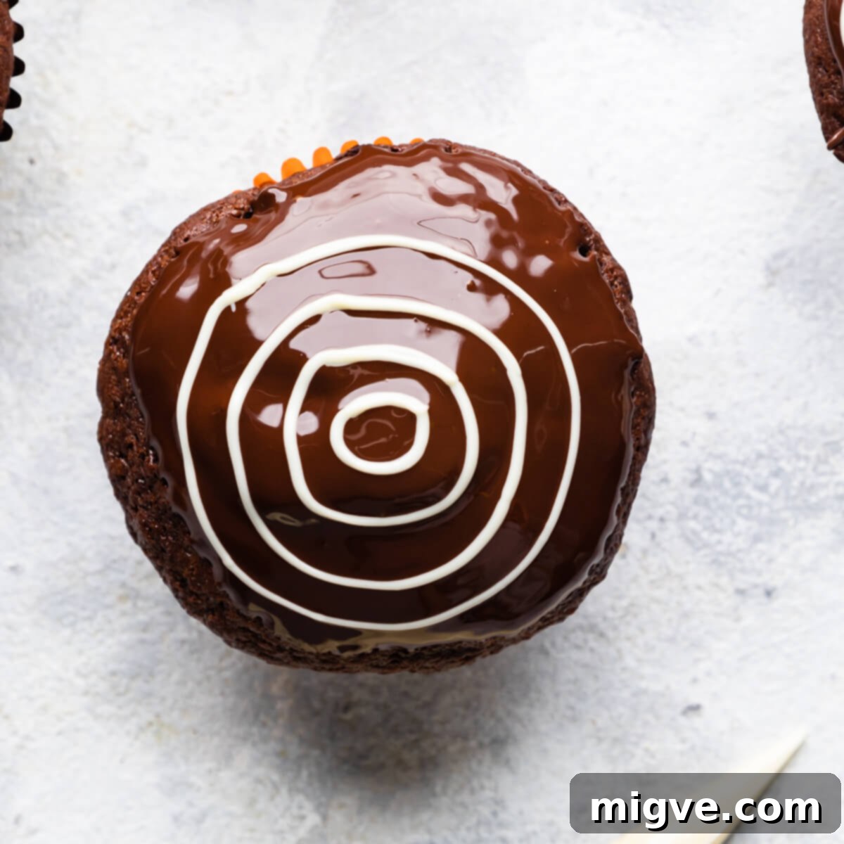 A freshly dipped chocolate muffin with concentric circles of white chocolate piped on top, forming the initial pattern for a spiderweb.