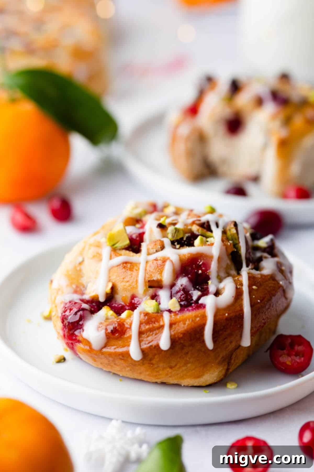 Close-up side view of an orange and cranberry Chelsea bun, generously coated with a glistening sugar glaze, highlighting its soft texture and inviting filling.