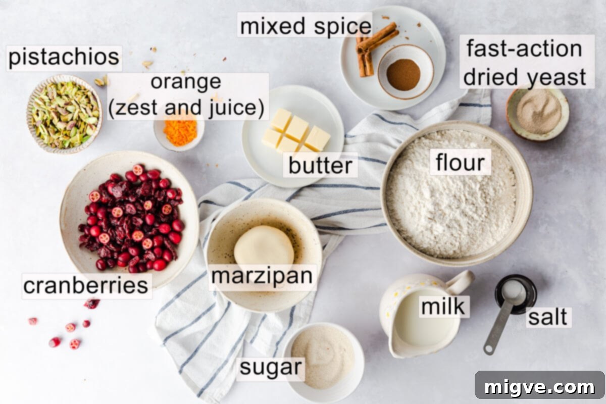 A selection of ingredients laid out, including flour, yeast, butter, milk, sugar, cranberries, oranges, marzipan, and pistachios, labeled for making Chelsea buns.