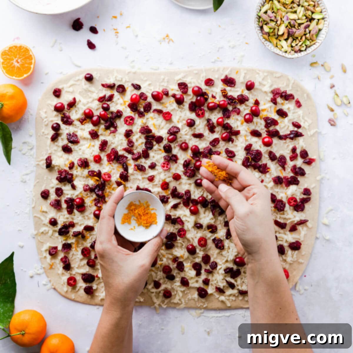Orange zest being sprinkled onto dough already topped with cranberries and marzipan, adding fresh citrus aroma to the Chelsea bun filling.