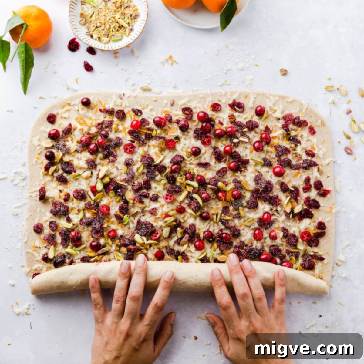 A sheet of dough, generously filled, being carefully rolled into a tight sausage or log shape, preparing to be sliced into individual Chelsea buns.