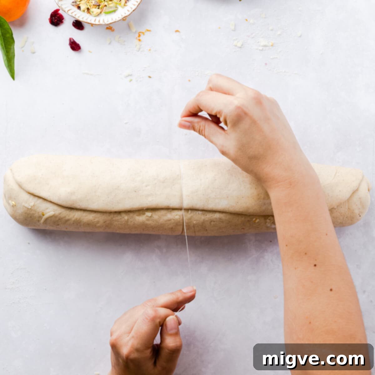 A log of Chelsea bun dough being expertly sliced into equal pieces using unflavored dental floss, ensuring neat and uniform buns.