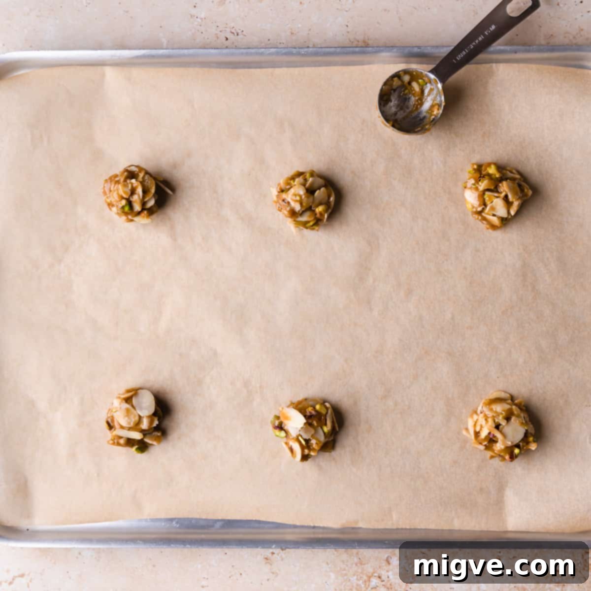 Florentine Almond Lace 7 Baking sheet lined with baking parchment, displaying small, rolled balls of almond florentine mixture and a measuring spoon for portioning.