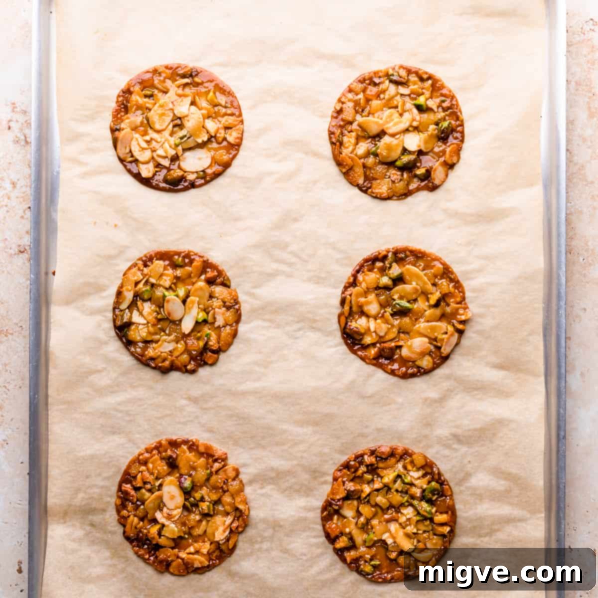 Florentine Almond Lace 10 Large metal baking sheet with six round, golden-brown almond and pistachio florentine cookies cooling after baking.
