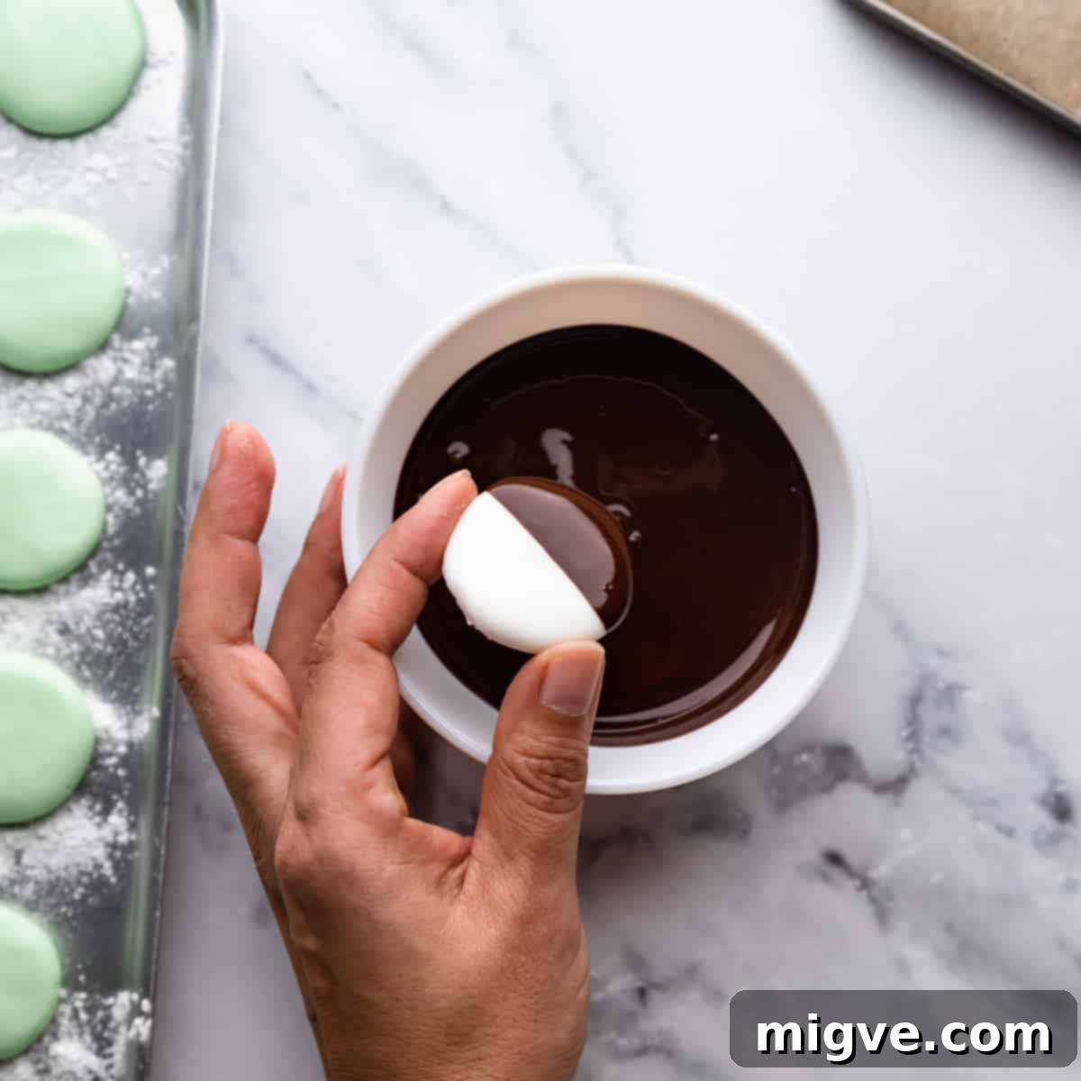 an individual mint cream being dipped in a small white bowl with melted chocolate.