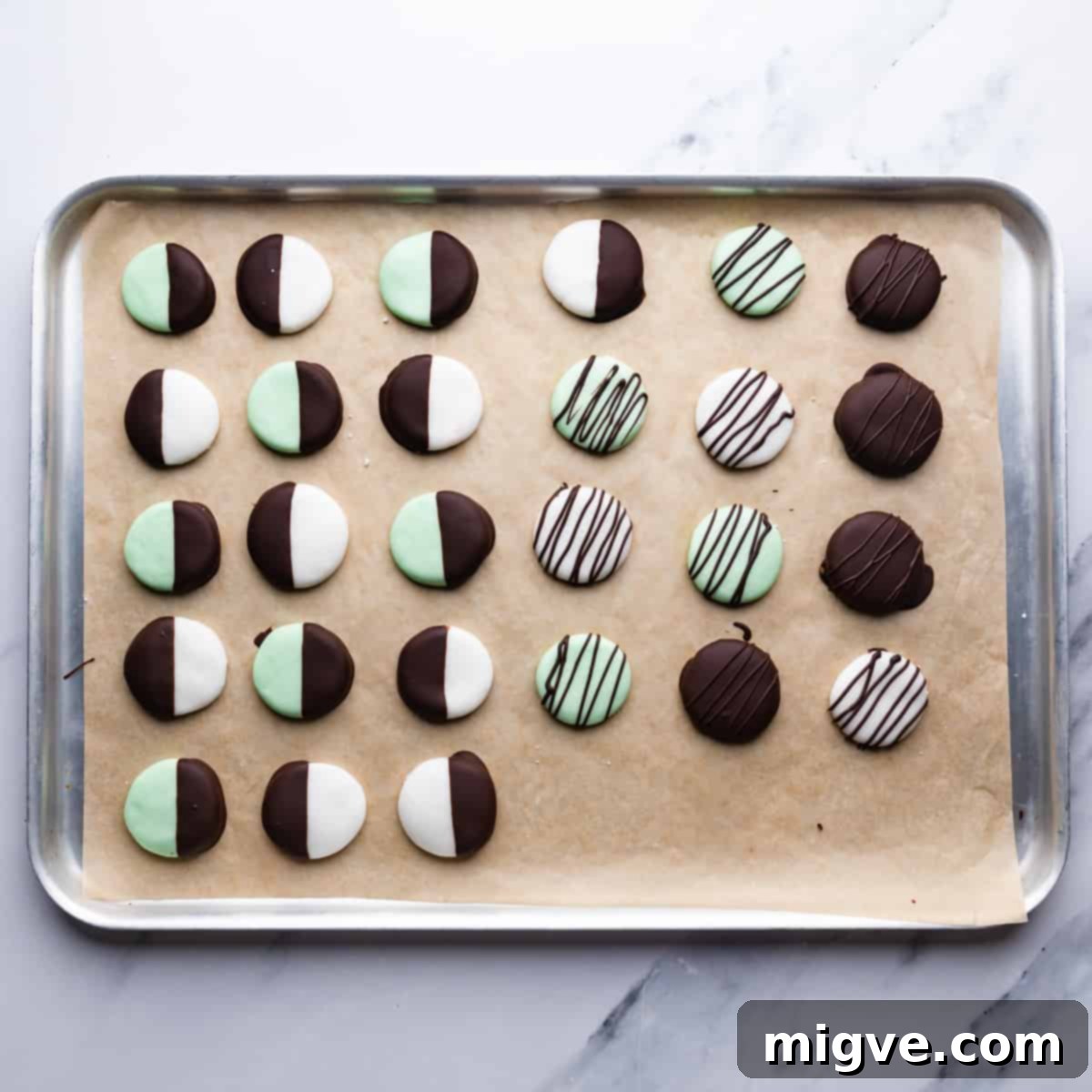 discs of mint creams dipped and drizzled with chocolate on a silver metal tray lined with brown baking paper.