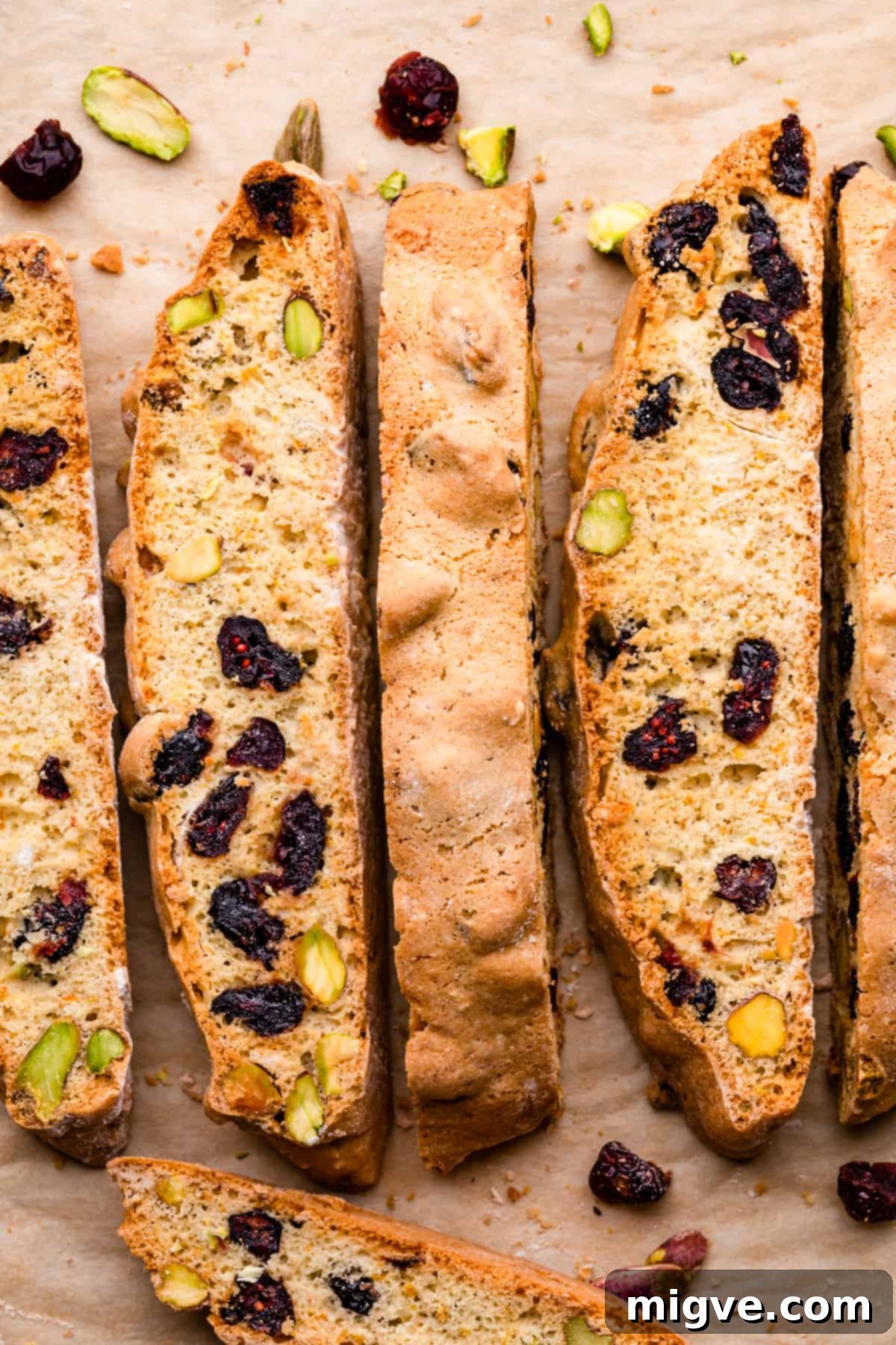 Ruby Red Biscotti 10 crispy cranberry biscotti slices with crushed pistachios and dried cranberries scattered around them.
