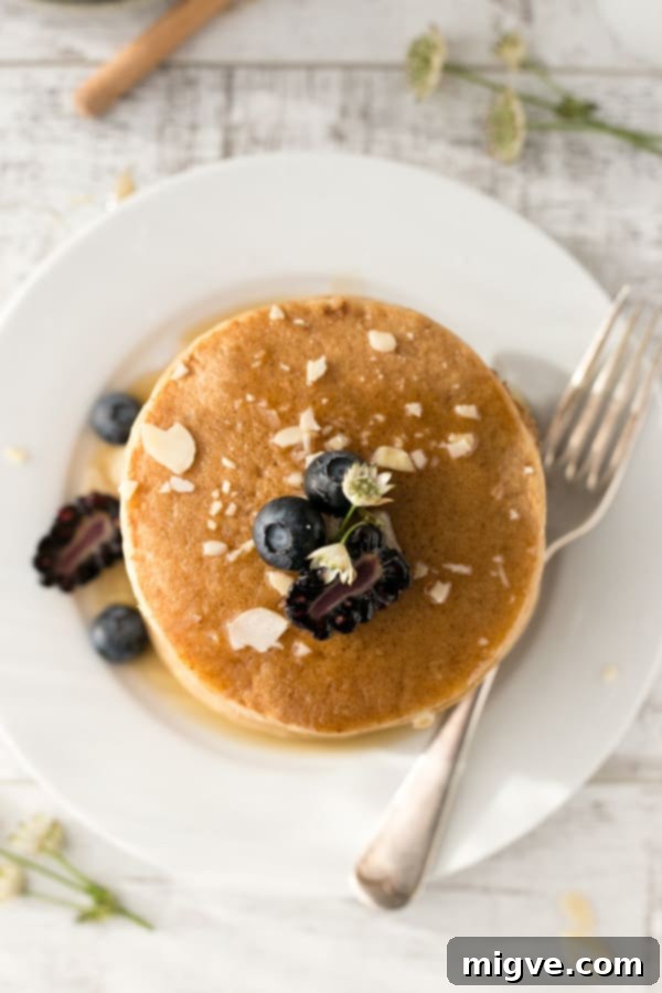 A towering stack of fluffy tofu pancakes generously drizzled with maple syrup, garnished with fresh fruit