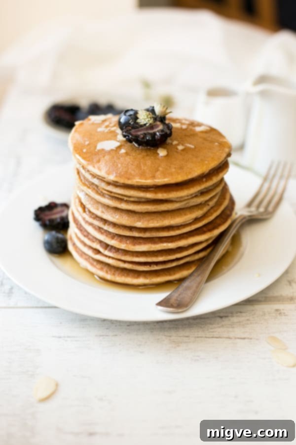 Close-up shot of a stack of fluffy tofu pancakes with a generous, glossy pour of maple syrup and delicate berries