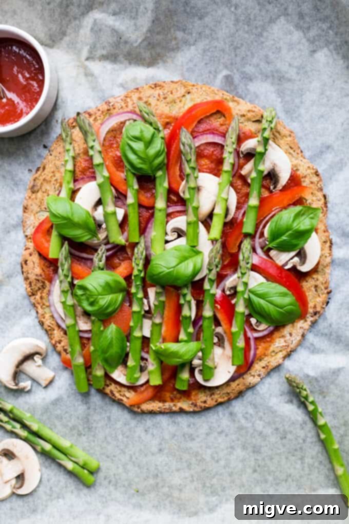 Close-up of a Cauliflower Pizza Crust featuring fresh asparagus and a luscious spinach dressing, emphasizing its fresh ingredients.