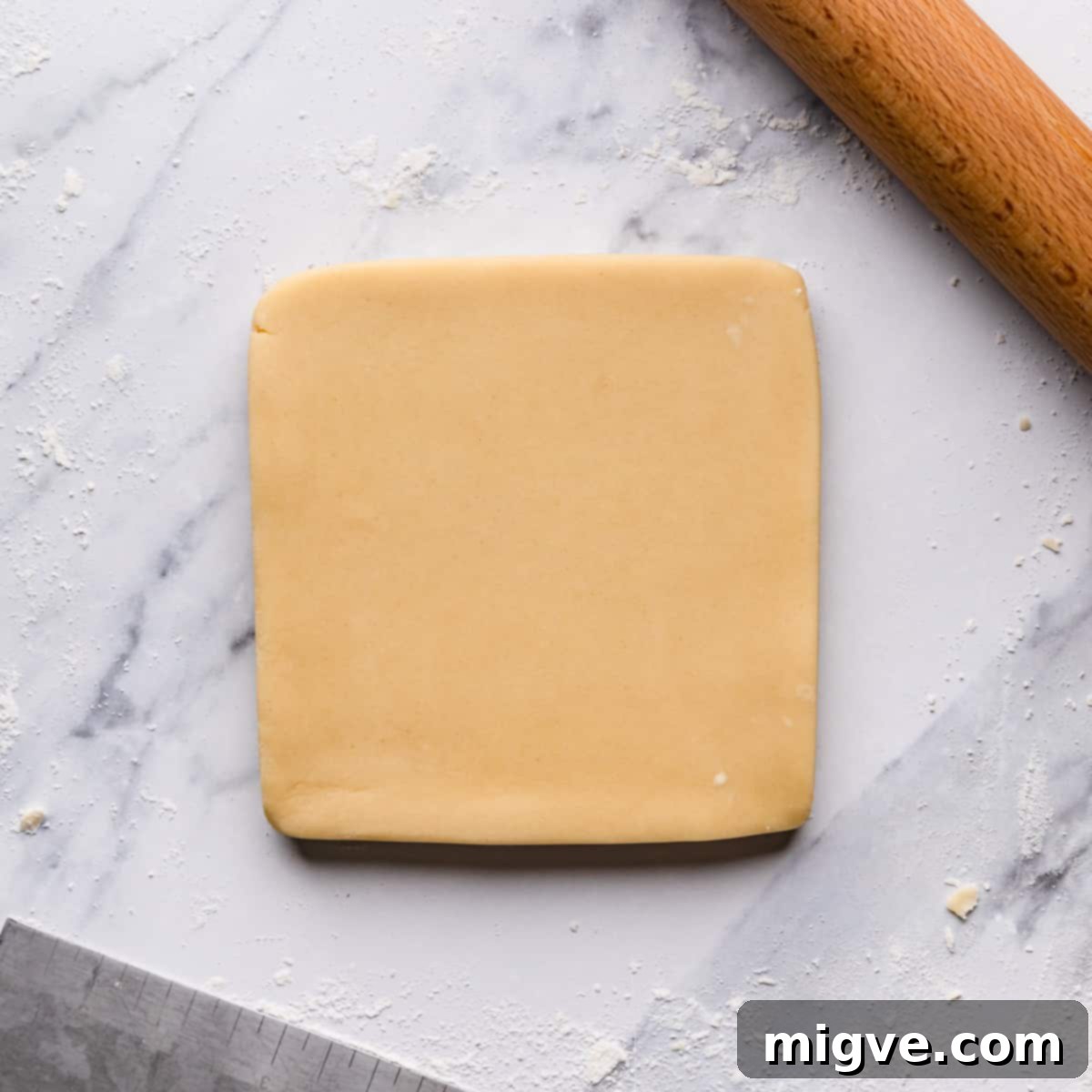 Smooth shortbread biscuit dough rolled into a square shape on a lightly floured surface.