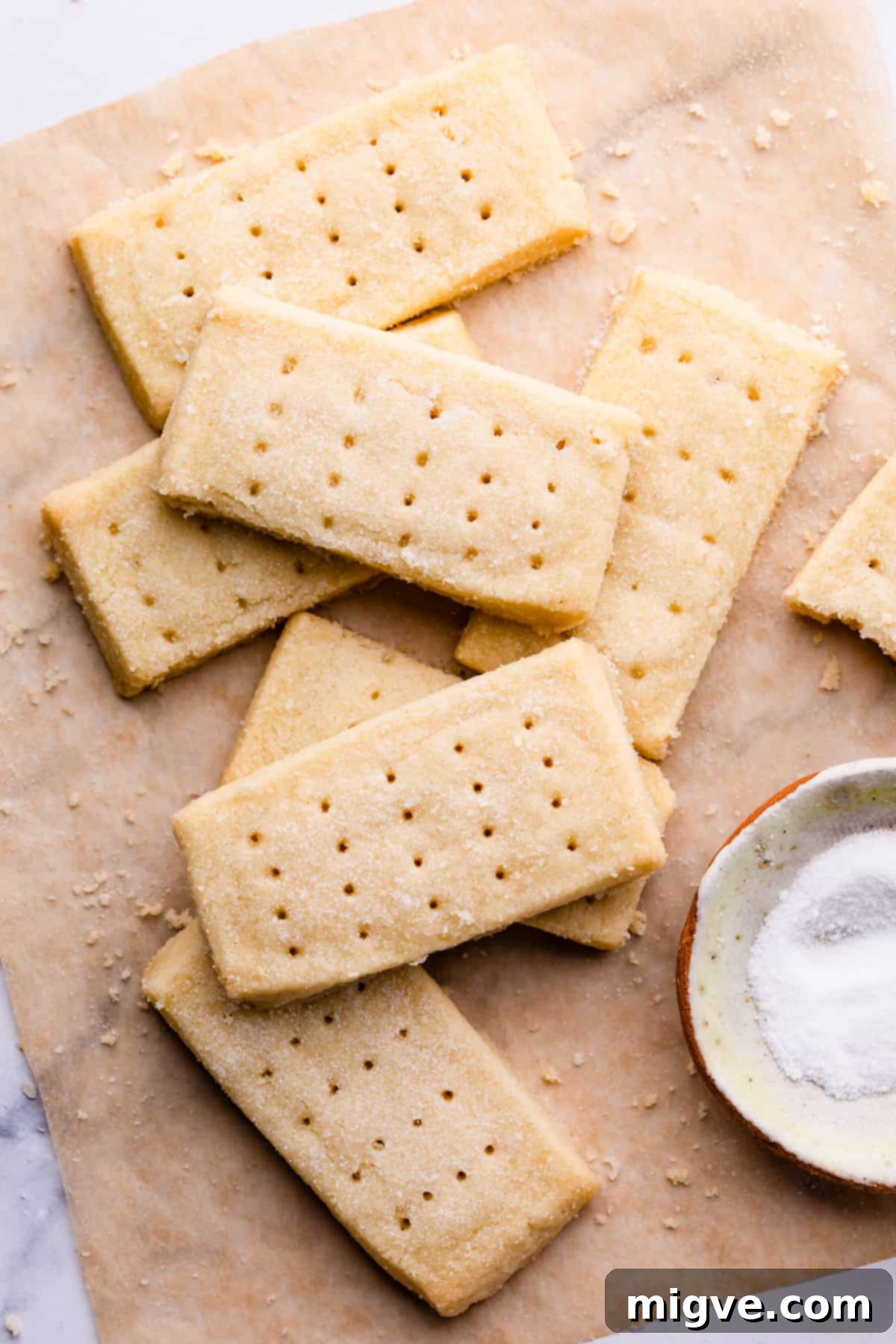 A batch of freshly baked shortbread biscuits on brown baking paper, surrounded by delicious crumbs.