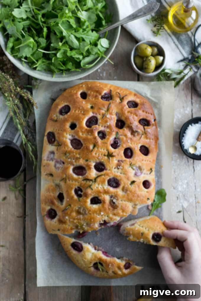 Traditional focaccia bread with aromatic rosemary and vibrant red grapes, ready to be enjoyed