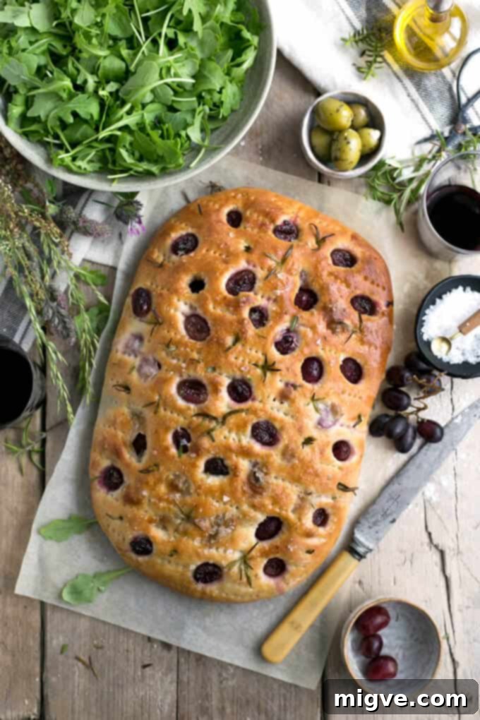 Close-up of rosemary focaccia with red grapes, sea salt, and a drizzle of olive oil, showcasing texture