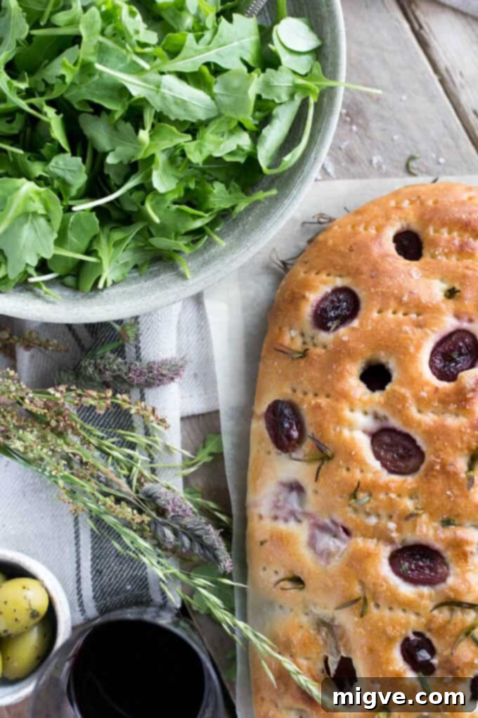 Rosemary focaccia bread, sliced and ready to serve, with red grapes and sea salt