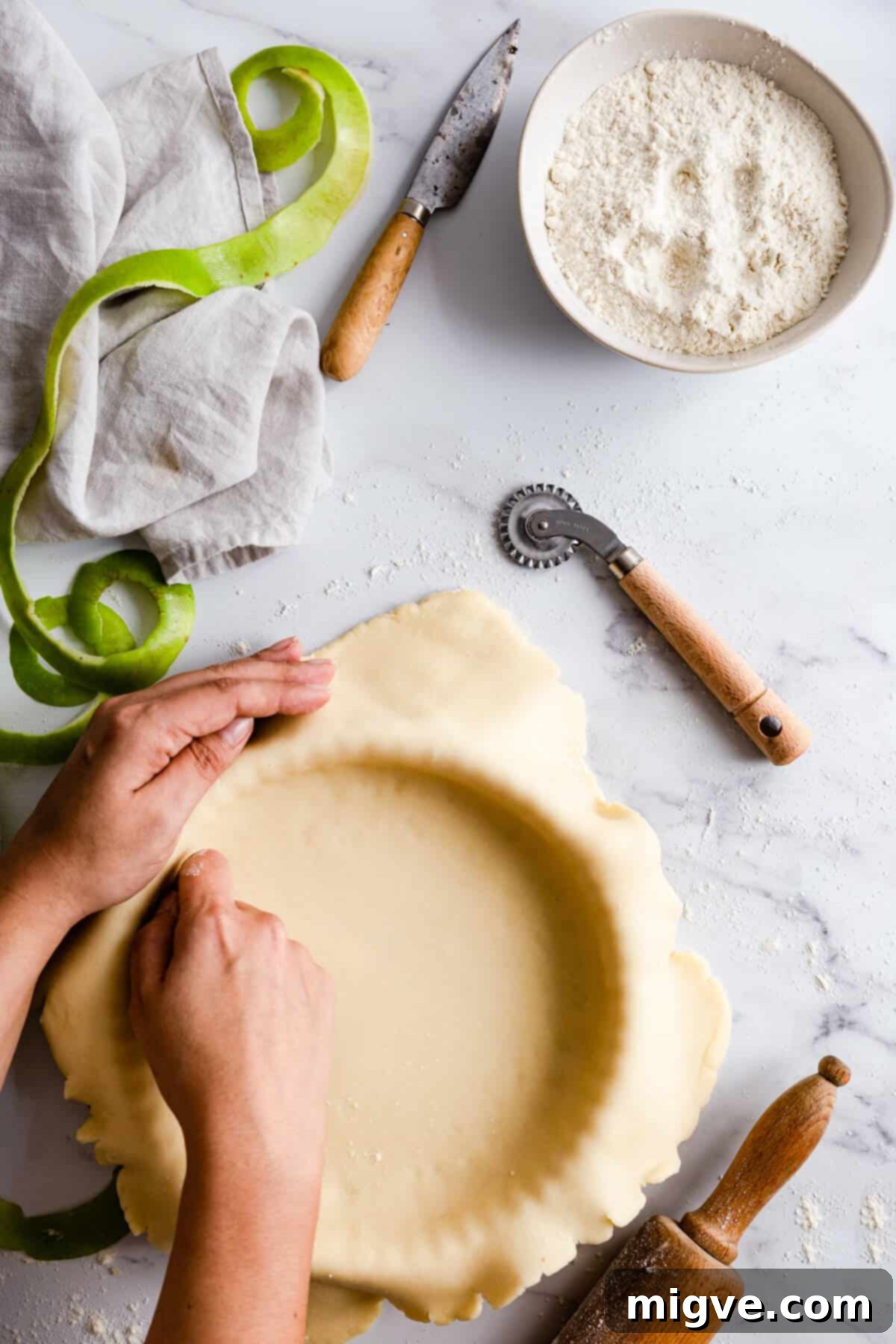 An overhead shot of a person carefully pressing rolled-out pastry into a round baking tin, ensuring it fits snugly along the edges.