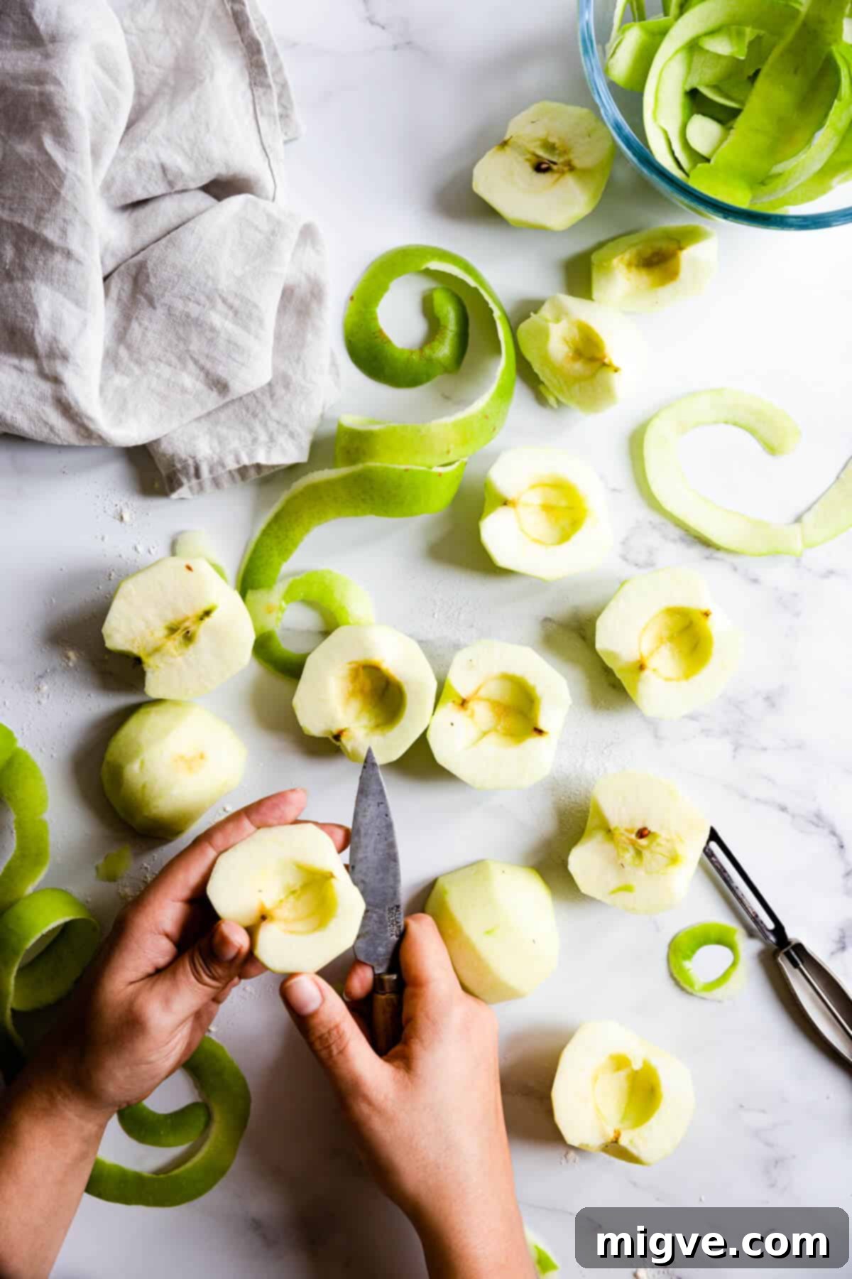 A person's hands skillfully peeling green apples over a bowl, preparing them for a delicious apple pie filling.