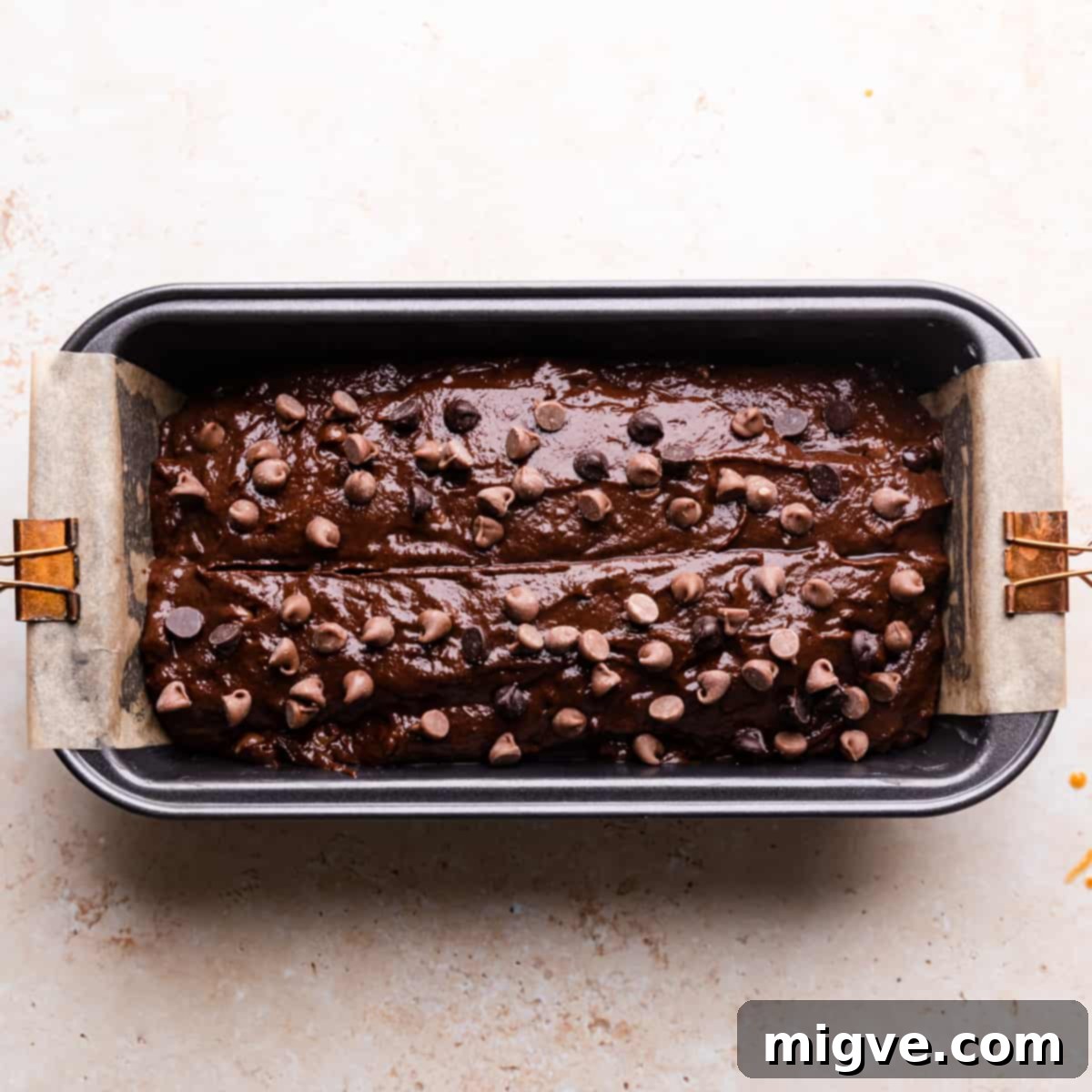 A loaf tin perfectly filled with the rich chocolate pumpkin bread batter, topped with extra chocolate chips, ready for baking.
