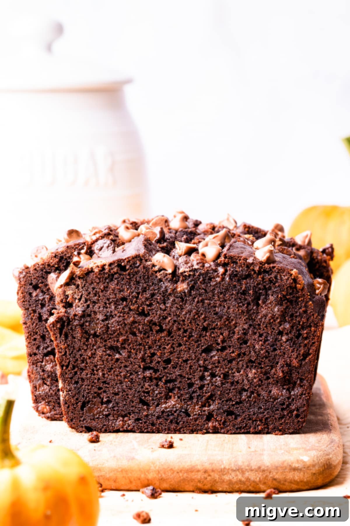 A freshly baked chocolate pumpkin bread loaf, adorned with a sprinkle of chocolate chips, resting on a small rustic wooden chopping board.