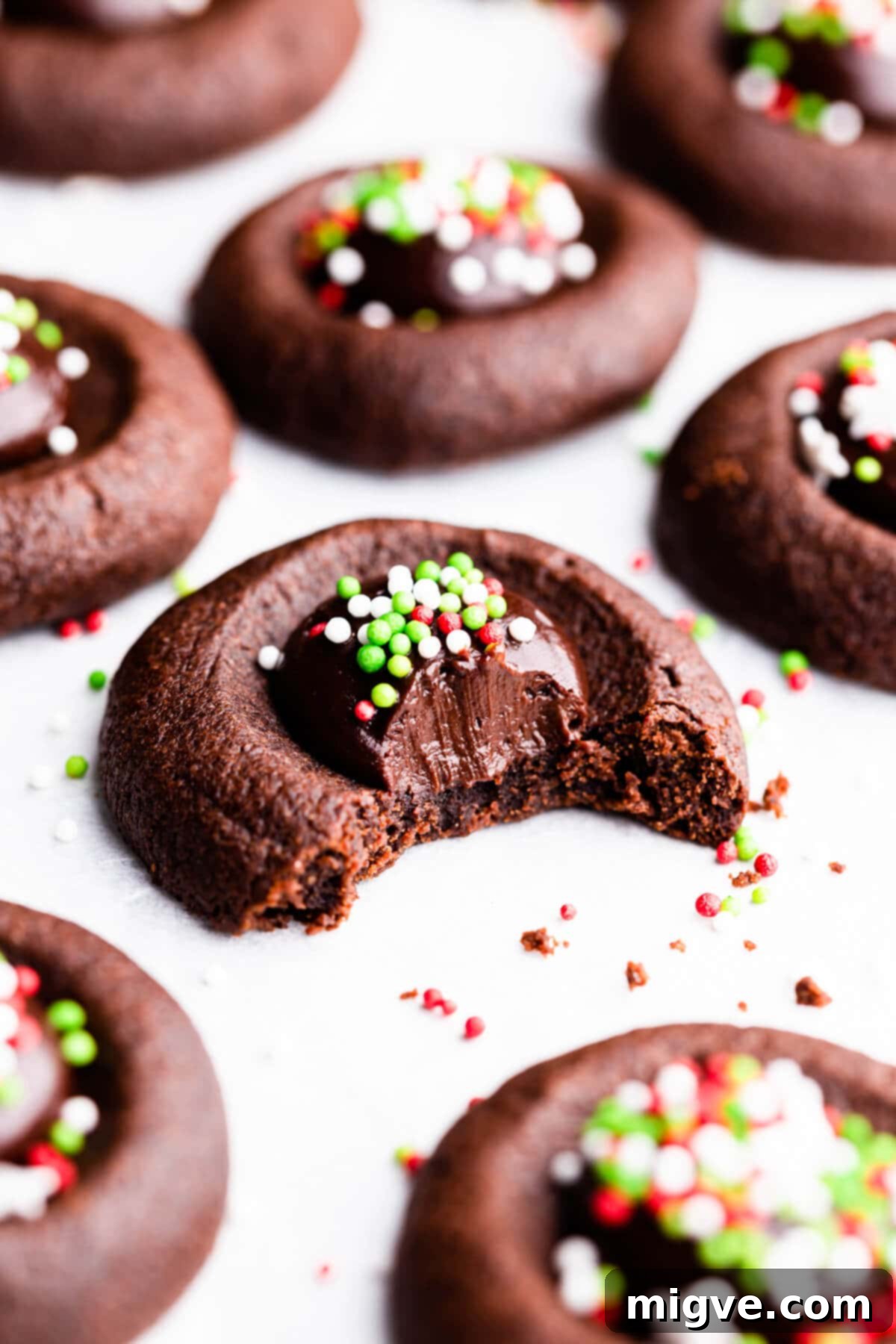 Super close-up side view of a single chocolate thumbprint cookie with a bite taken out, revealing the soft interior and creamy ganache filling.